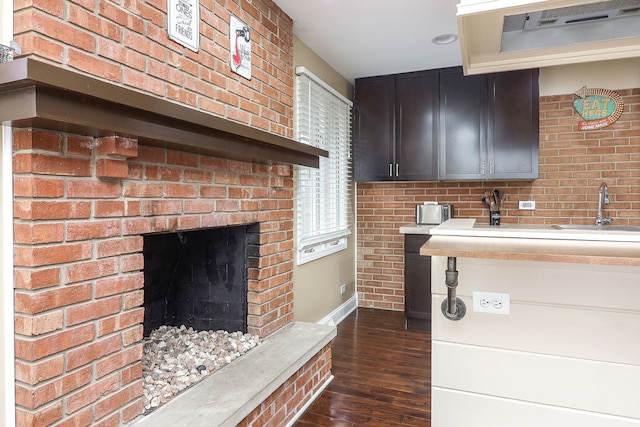 kitchen featuring a sink, a brick fireplace, extractor fan, light countertops, and dark wood-style flooring