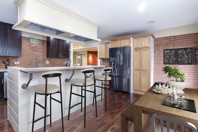 kitchen featuring a breakfast bar, dark wood-style floors, black fridge, and light countertops