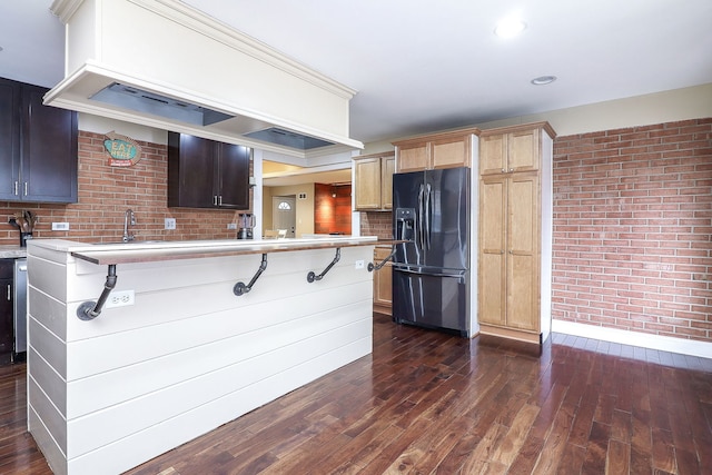 kitchen with premium range hood, brick wall, dark wood-type flooring, light countertops, and black fridge with ice dispenser