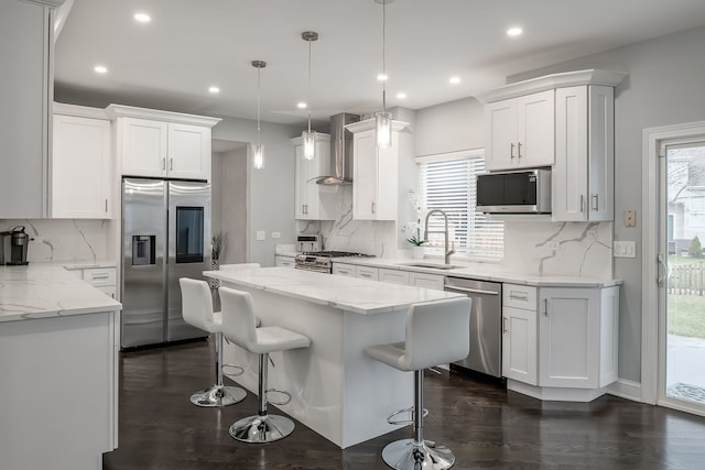 kitchen with a center island, stainless steel appliances, white cabinets, a sink, and wall chimney range hood