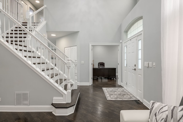 foyer entrance with dark wood-type flooring, baseboards, visible vents, and a high ceiling