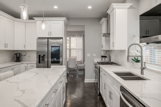 kitchen featuring light stone counters, decorative light fixtures, appliances with stainless steel finishes, white cabinets, and a sink