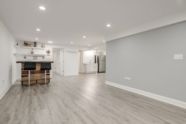 living area featuring recessed lighting, bar, light wood-style flooring, and baseboards