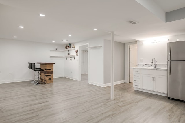 finished basement with visible vents, light wood-style flooring, freestanding refrigerator, a bar, and a sink