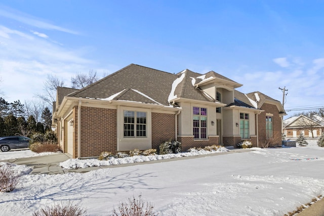 view of front of property featuring a garage, stucco siding, a shingled roof, and brick siding