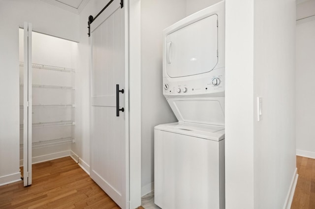 laundry area with laundry area, a barn door, baseboards, light wood-style flooring, and stacked washer / drying machine