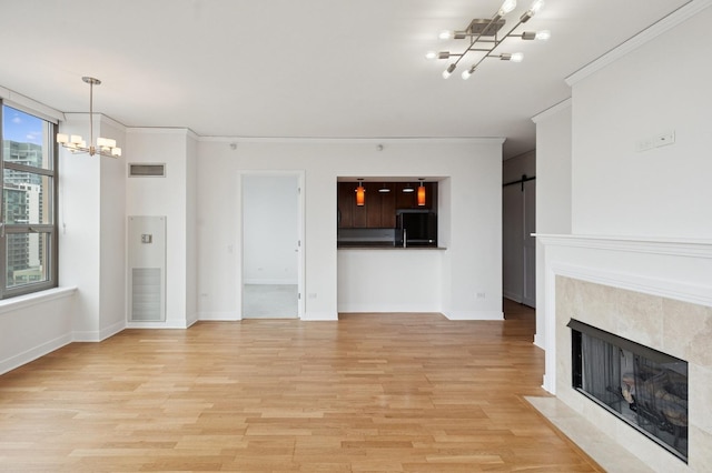 unfurnished living room with a barn door, visible vents, a tiled fireplace, an inviting chandelier, and light wood-type flooring