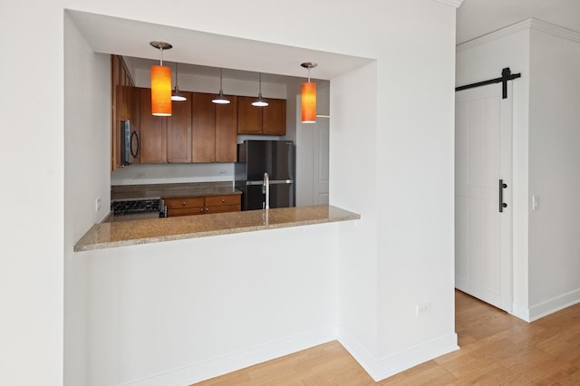 kitchen featuring a peninsula, a barn door, light wood-style flooring, and freestanding refrigerator