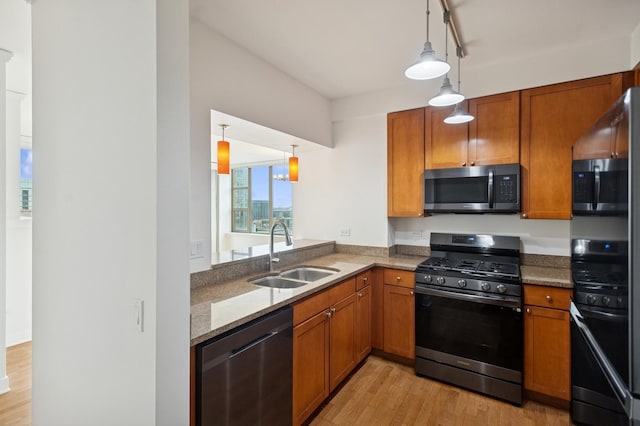 kitchen with stone countertops, stainless steel appliances, a sink, light wood finished floors, and brown cabinetry