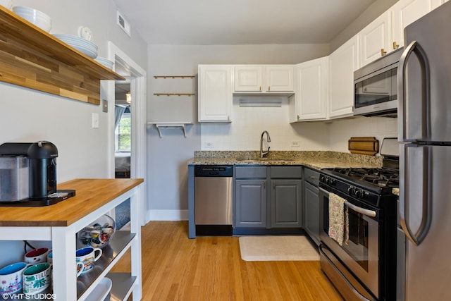 kitchen with a sink, white cabinets, appliances with stainless steel finishes, and light wood-style flooring