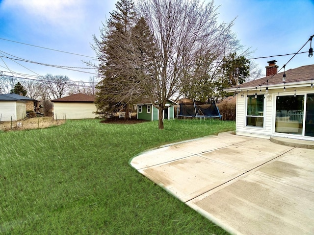 view of yard featuring a trampoline, a patio, and an outbuilding