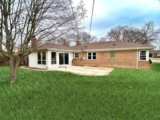 rear view of house featuring brick siding, a yard, a chimney, concrete driveway, and a patio area