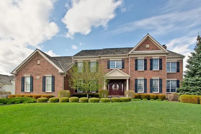 view of front of home featuring brick siding, a chimney, and a front yard