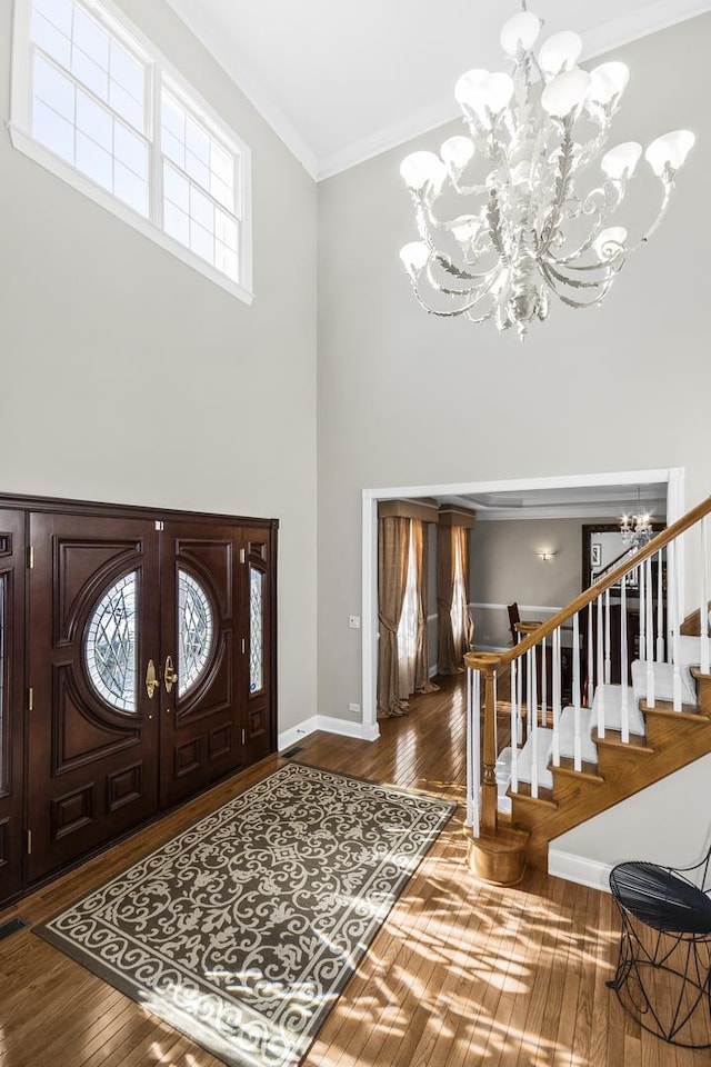 foyer entrance featuring hardwood / wood-style flooring, a notable chandelier, a high ceiling, ornamental molding, and stairway