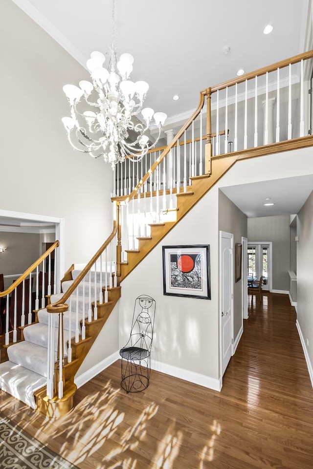 staircase featuring crown molding, a towering ceiling, baseboards, and wood finished floors