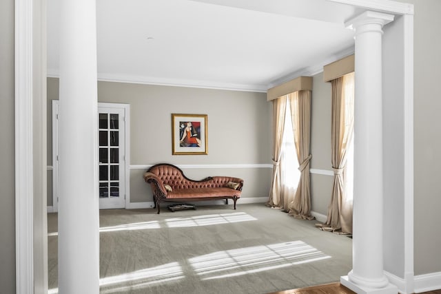 living area featuring baseboards, ornamental molding, decorative columns, and light colored carpet