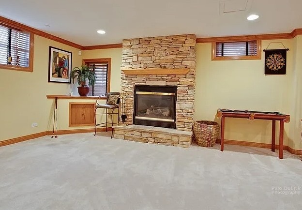 interior space featuring light carpet, ornamental molding, a fireplace, and baseboards