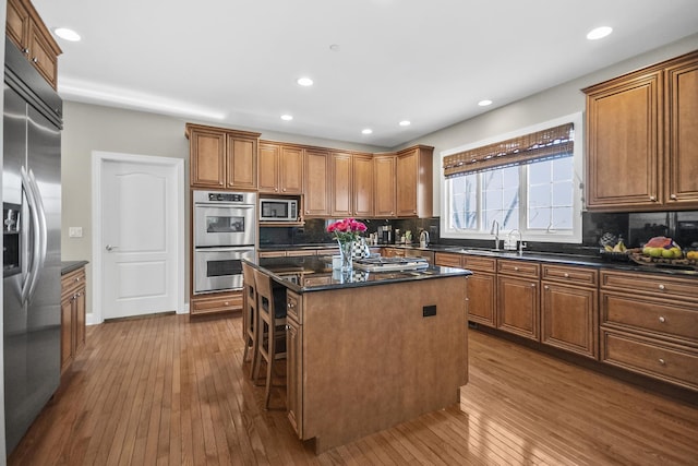 kitchen featuring built in appliances, a sink, a kitchen island, brown cabinetry, and wood-type flooring