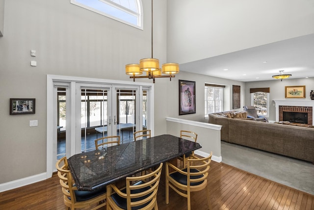 dining area with baseboards, a towering ceiling, dark wood-style flooring, french doors, and a fireplace