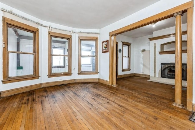 unfurnished room with wood-type flooring, a large fireplace, decorative columns, and baseboards