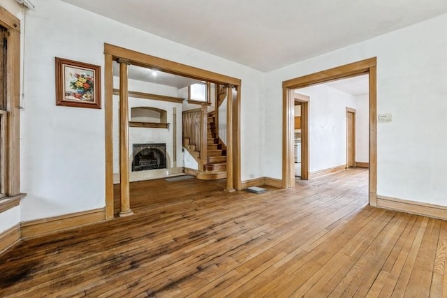 unfurnished room featuring a fireplace with raised hearth, stairs, light wood-style flooring, and baseboards