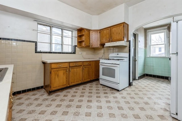 kitchen featuring tile walls, open shelves, brown cabinetry, white appliances, and under cabinet range hood