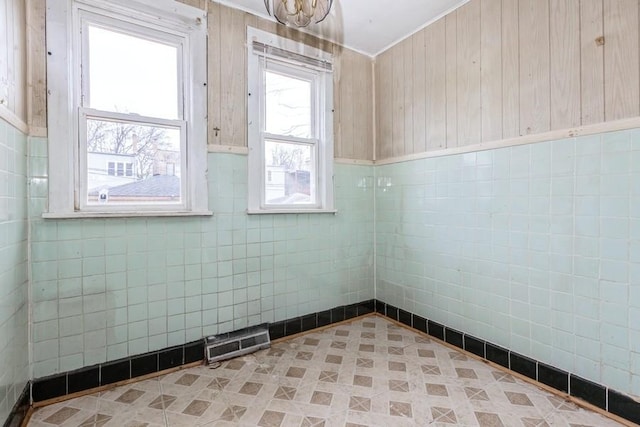 empty room featuring ornamental molding, a wainscoted wall, visible vents, and tile walls