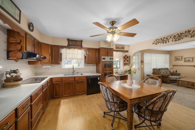 kitchen with light wood finished floors, arched walkways, a sink, decorative backsplash, and black appliances