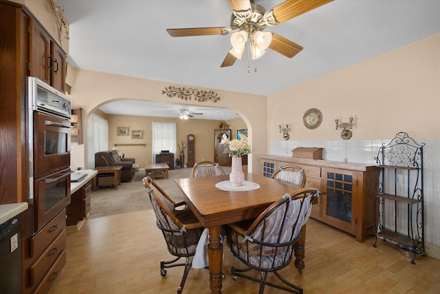 dining room featuring a ceiling fan, arched walkways, and light wood-type flooring