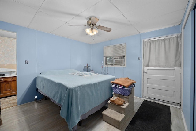 bedroom with light wood-type flooring, cooling unit, a drop ceiling, and a ceiling fan