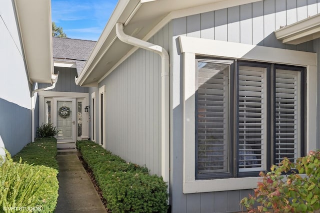 view of exterior entry featuring roof with shingles and fence