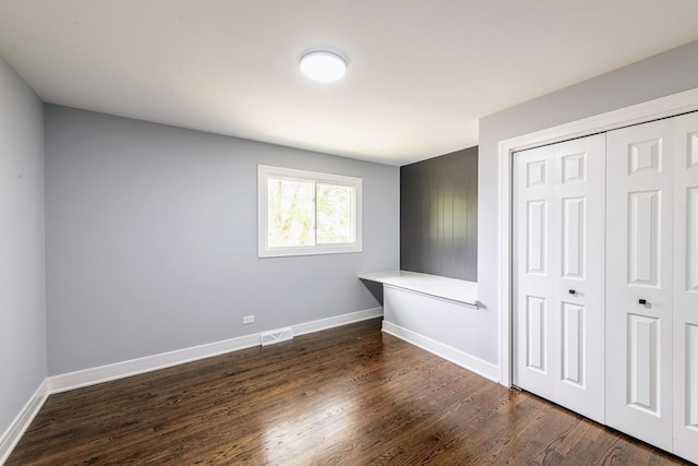 unfurnished bedroom with dark wood-type flooring, a closet, visible vents, and baseboards