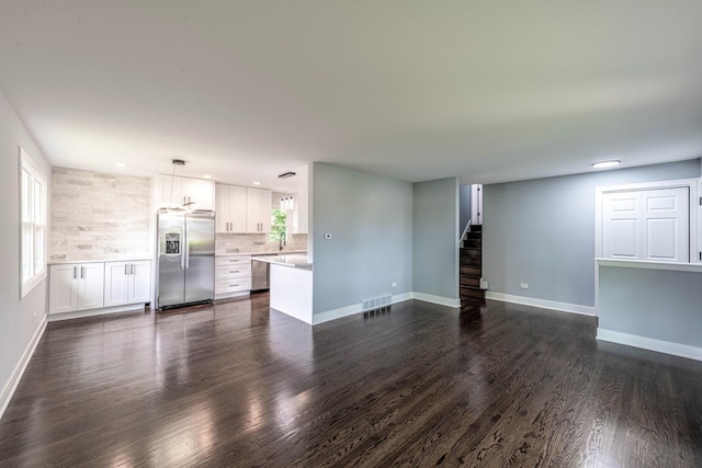 unfurnished living room with dark wood-style floors, visible vents, a sink, baseboards, and stairs