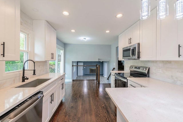 kitchen with light stone counters, decorative light fixtures, appliances with stainless steel finishes, white cabinets, and a sink