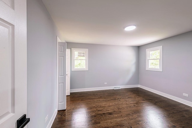 spare room with dark wood-style floors, visible vents, and baseboards