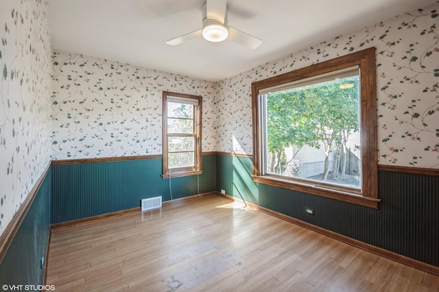 spare room with a wainscoted wall, visible vents, a ceiling fan, wood finished floors, and wallpapered walls