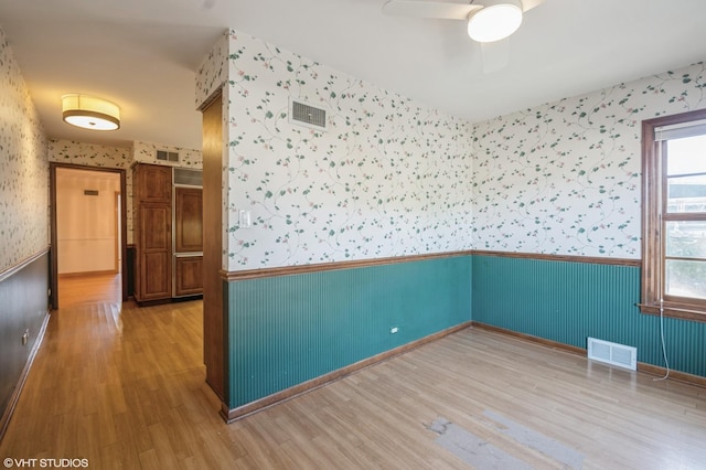 empty room with wallpapered walls, visible vents, a wainscoted wall, and wood finished floors