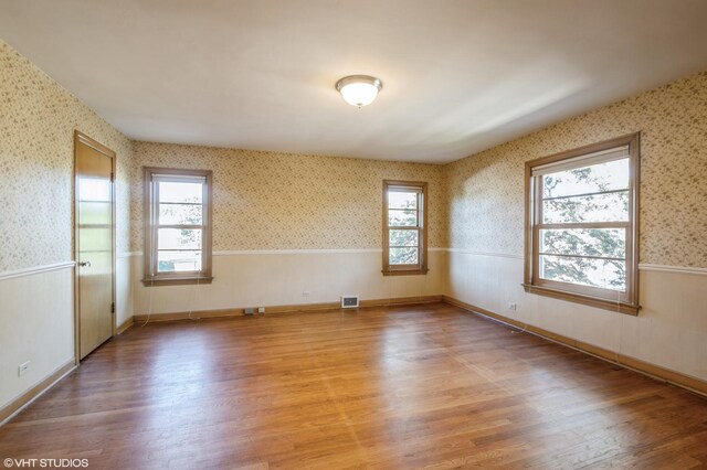 spare room with wallpapered walls, visible vents, a wainscoted wall, and wood finished floors