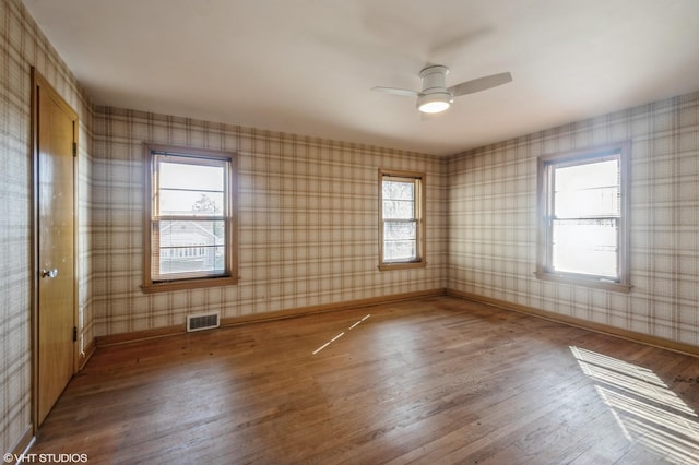 spare room with wallpapered walls, baseboards, visible vents, ceiling fan, and wood finished floors