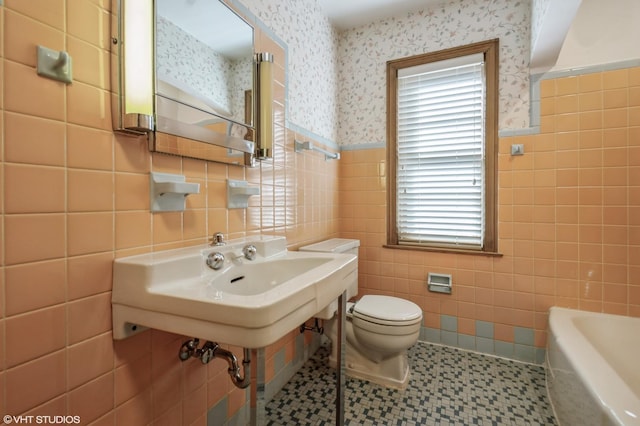 bathroom with toilet, wallpapered walls, a washtub, and a wainscoted wall