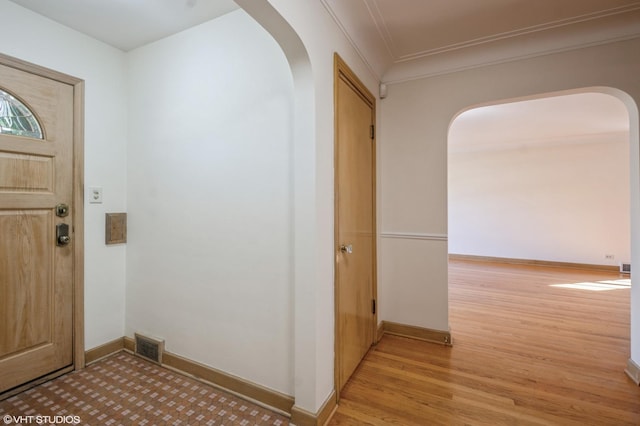 foyer entrance with ornamental molding, light wood-type flooring, visible vents, and baseboards