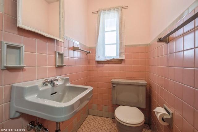 half bathroom with wainscoting, a sink, toilet, and tile walls