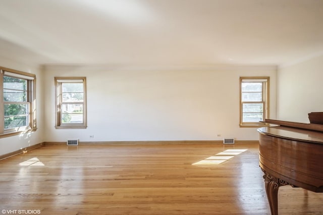 unfurnished room with light wood finished floors, visible vents, and a wealth of natural light