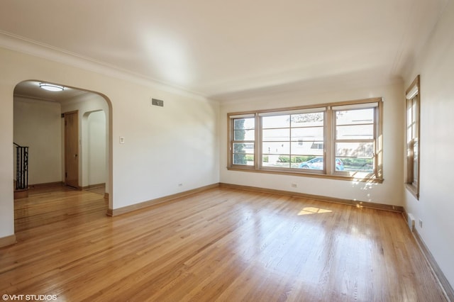 spare room with visible vents, arched walkways, baseboards, ornamental molding, and light wood-type flooring