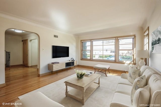 living room featuring visible vents, arched walkways, baseboards, ornamental molding, and light wood-type flooring