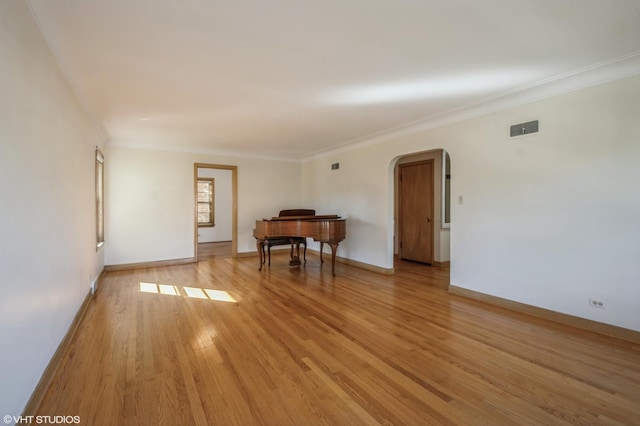 empty room featuring light wood finished floors, visible vents, arched walkways, baseboards, and crown molding