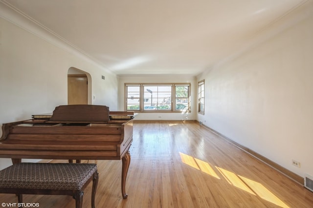 living room with arched walkways, visible vents, baseboards, light wood finished floors, and crown molding