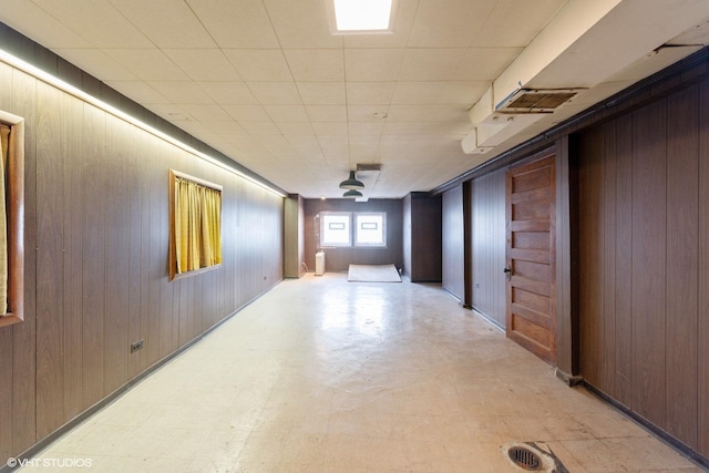 hall with light floors, wooden walls, visible vents, and a drop ceiling