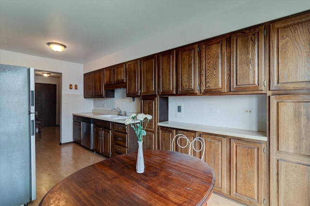 kitchen featuring dark brown cabinetry, a sink, light countertops, stainless steel dishwasher, and freestanding refrigerator