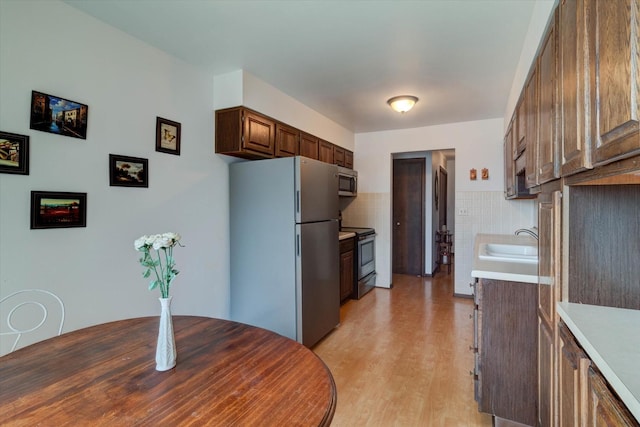 kitchen with stainless steel appliances, a sink, light countertops, decorative backsplash, and light wood finished floors